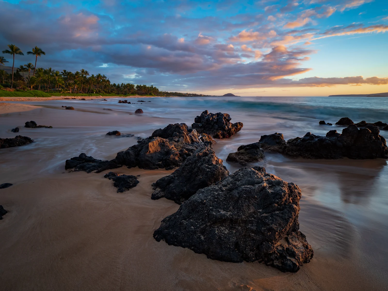Sunset sky, palms and waves around lava rocks at Keawakapu Beach, Maui