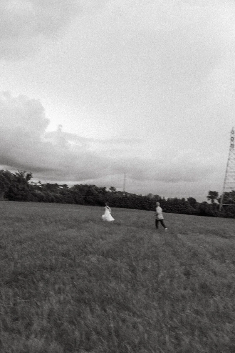 A softly blurred black-and-white photograph of a couple running through a field.