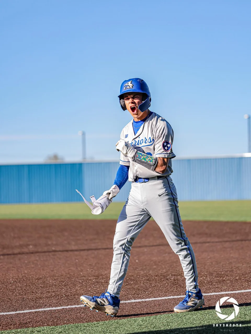 A baseball player in a blue helmet and gray uniform reacts on the field.