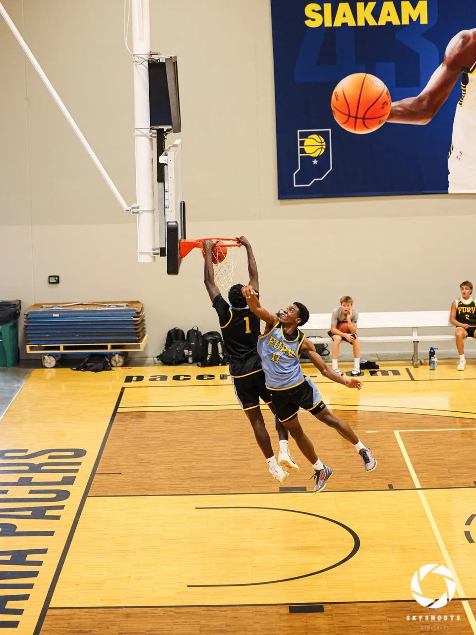A basketball player in a dark uniform attacks the basket while a defender contests the play on an indoor court.