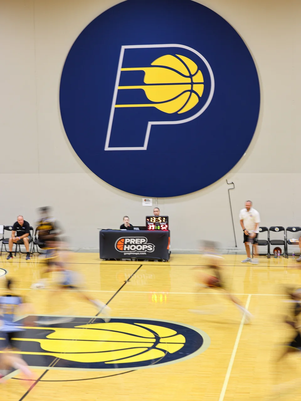 Motion-blurred basketball players cross a court beneath a large Pacers wall logo; the scorer table visibly carries Prep Hoops branding.