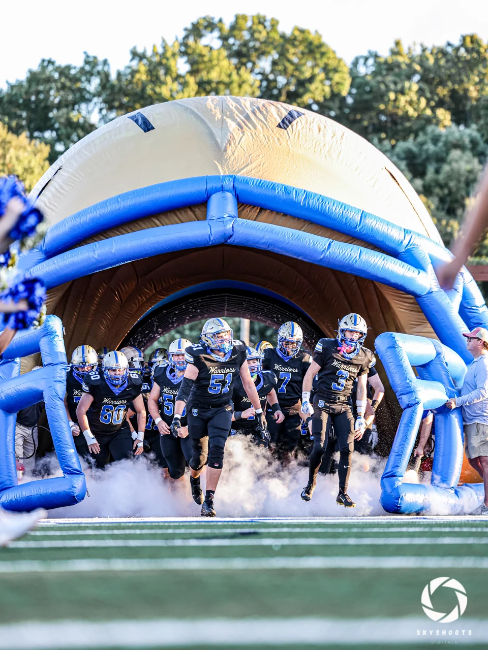 A football team runs onto the field through a large inflatable helmet.