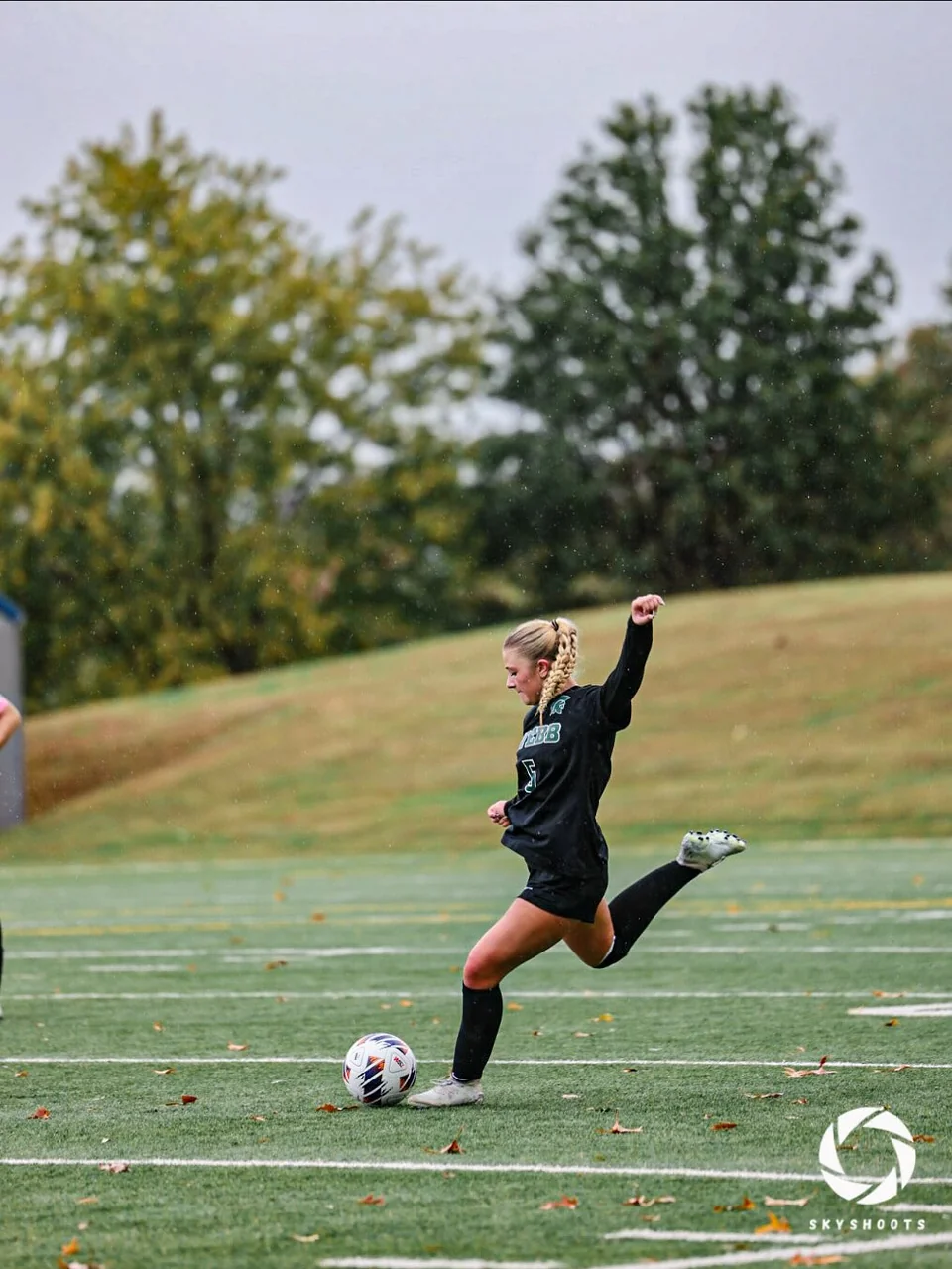 A soccer player in a dark uniform draws a leg back to strike the ball on the field.