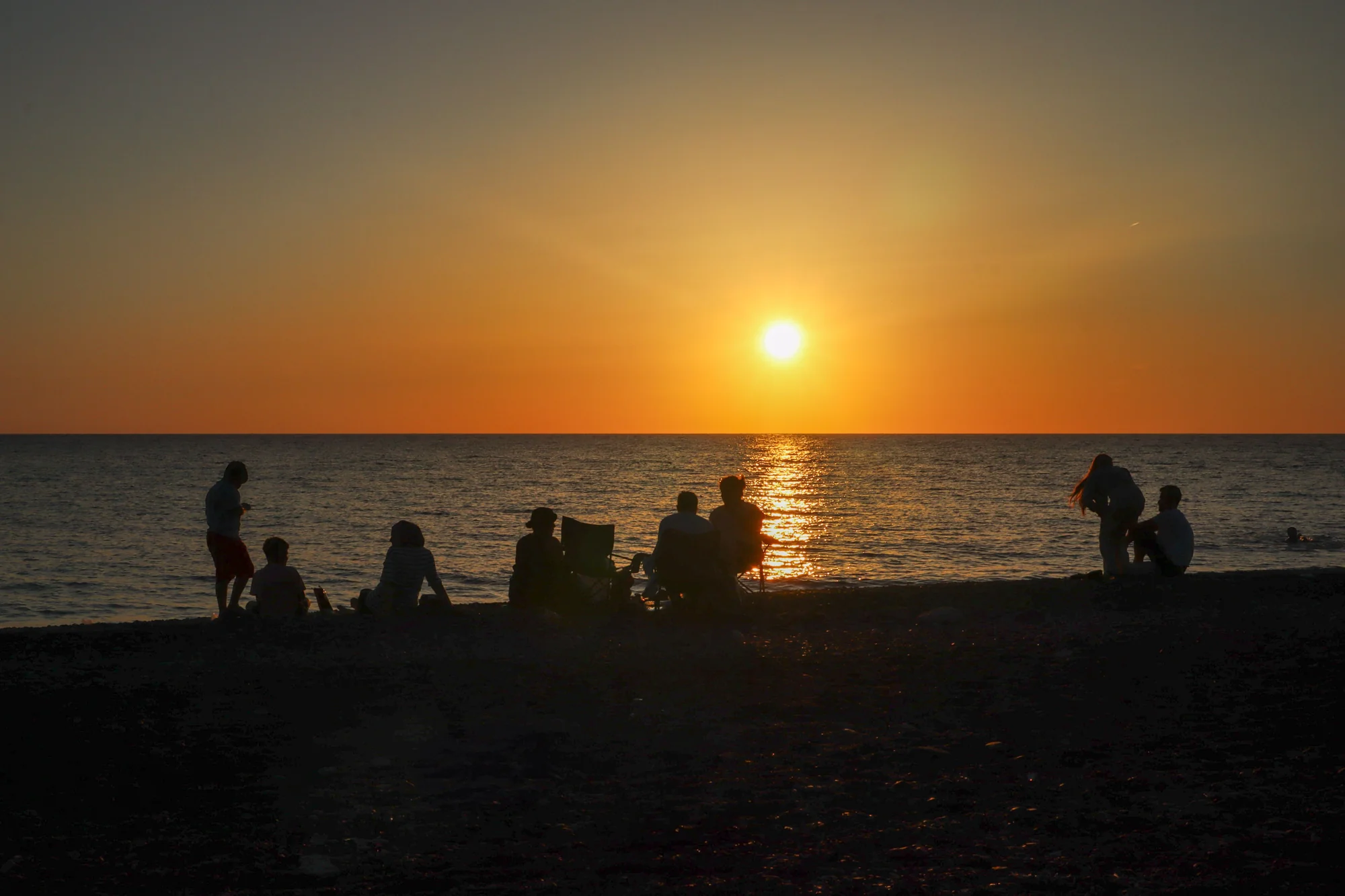 Small groups of people silhouetted along a beach at sunset